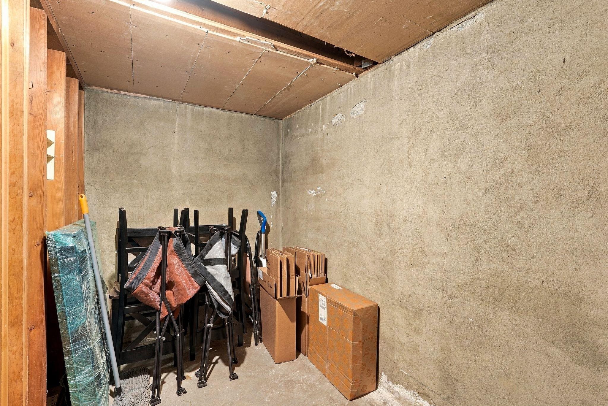 Basement storage area with concrete walls, folded chairs, and cardboard boxes.