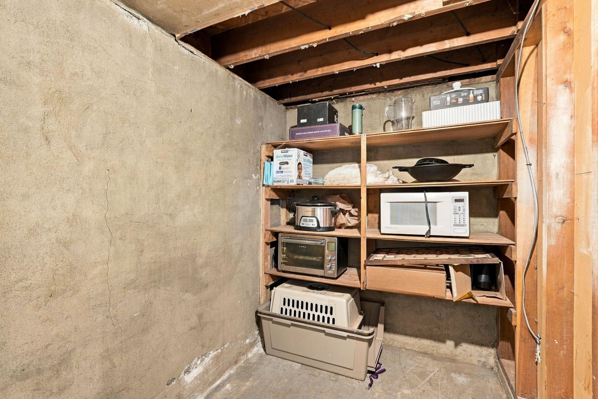 Basement storage area with exposed joists, concrete walls, and shelves of household items and appliances.