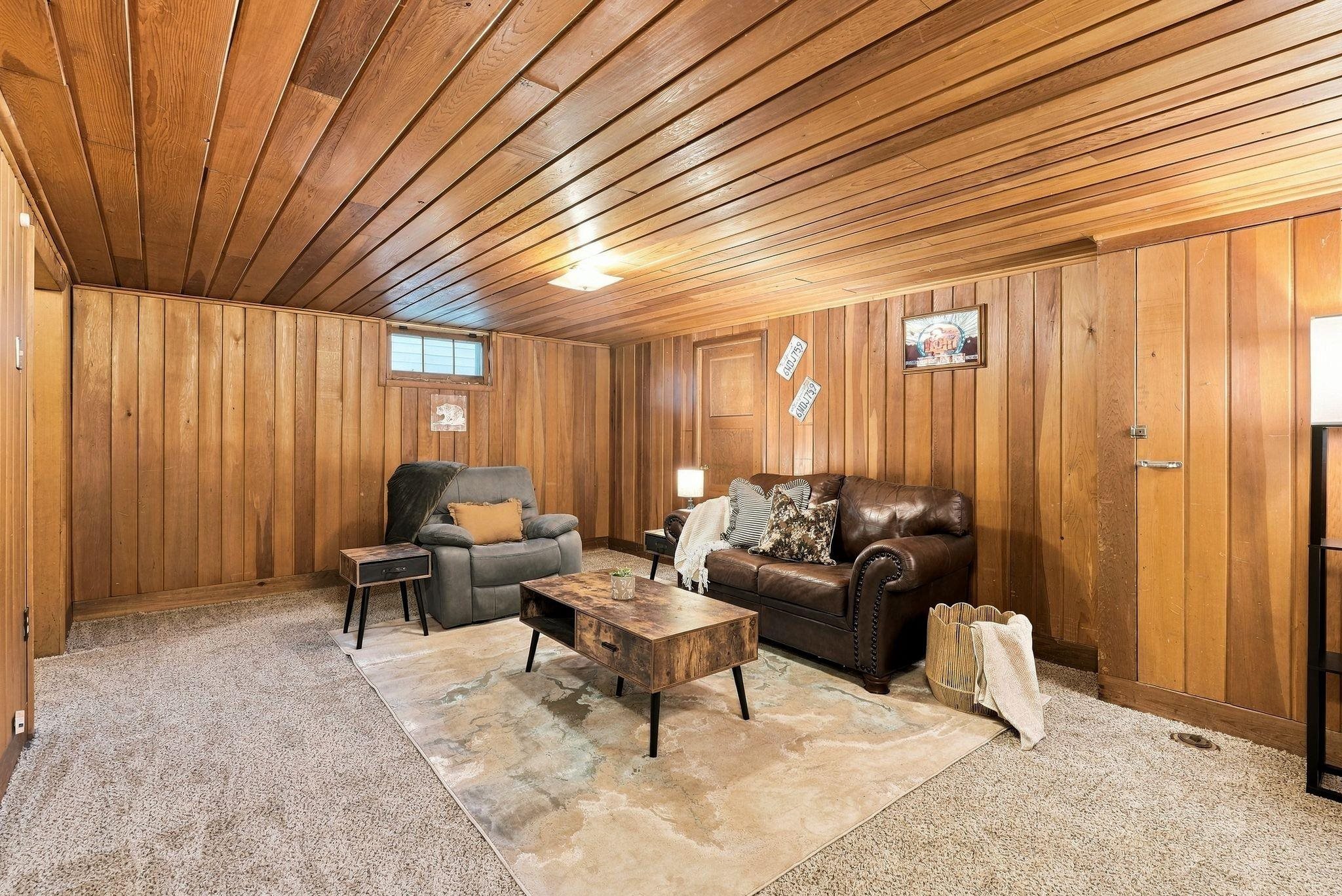 Wood-paneled living room with a leather sofa, recliner, and coffee table on a large rug.