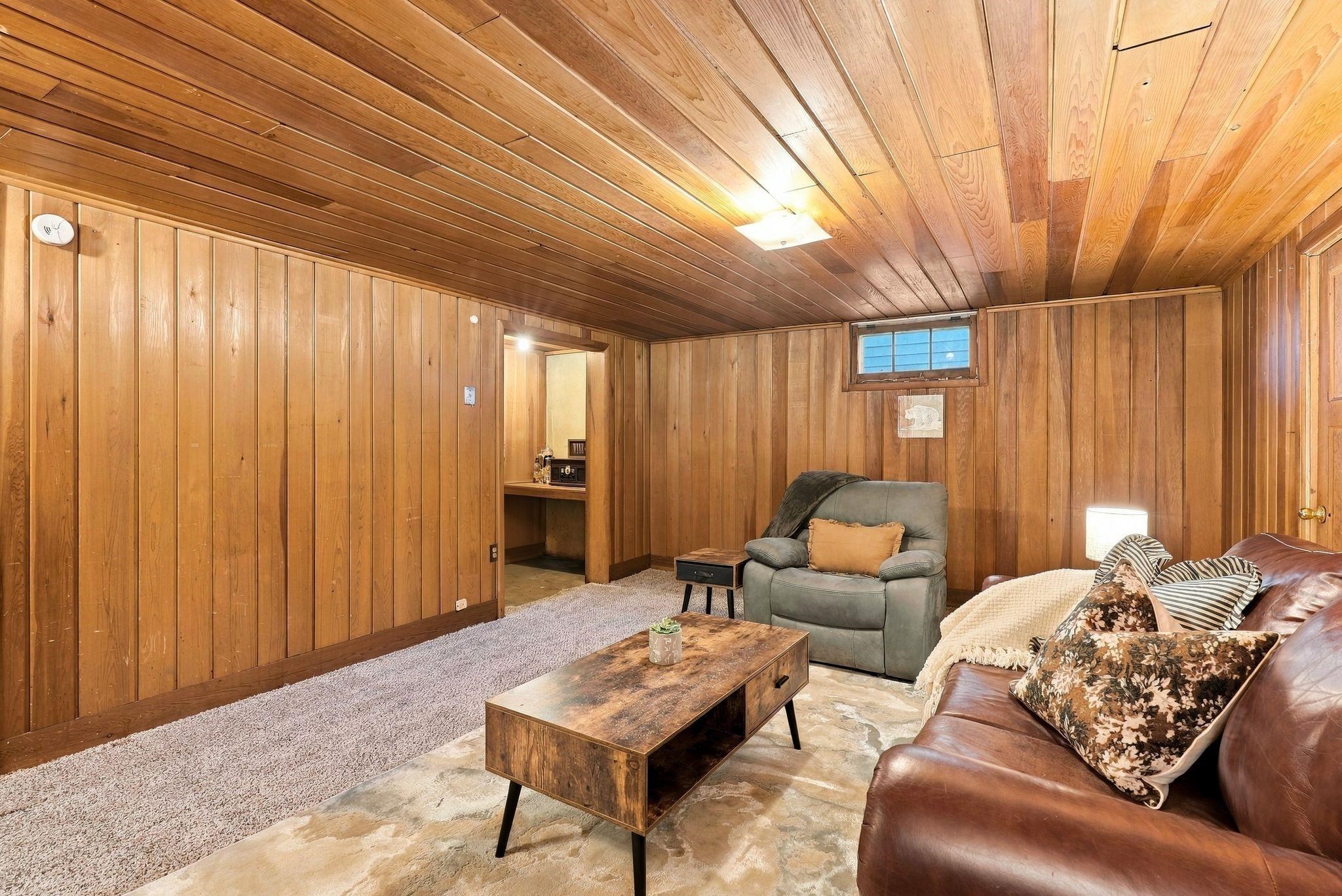 Wood-paneled living room with leather sofa, recliner, and rustic coffee table.