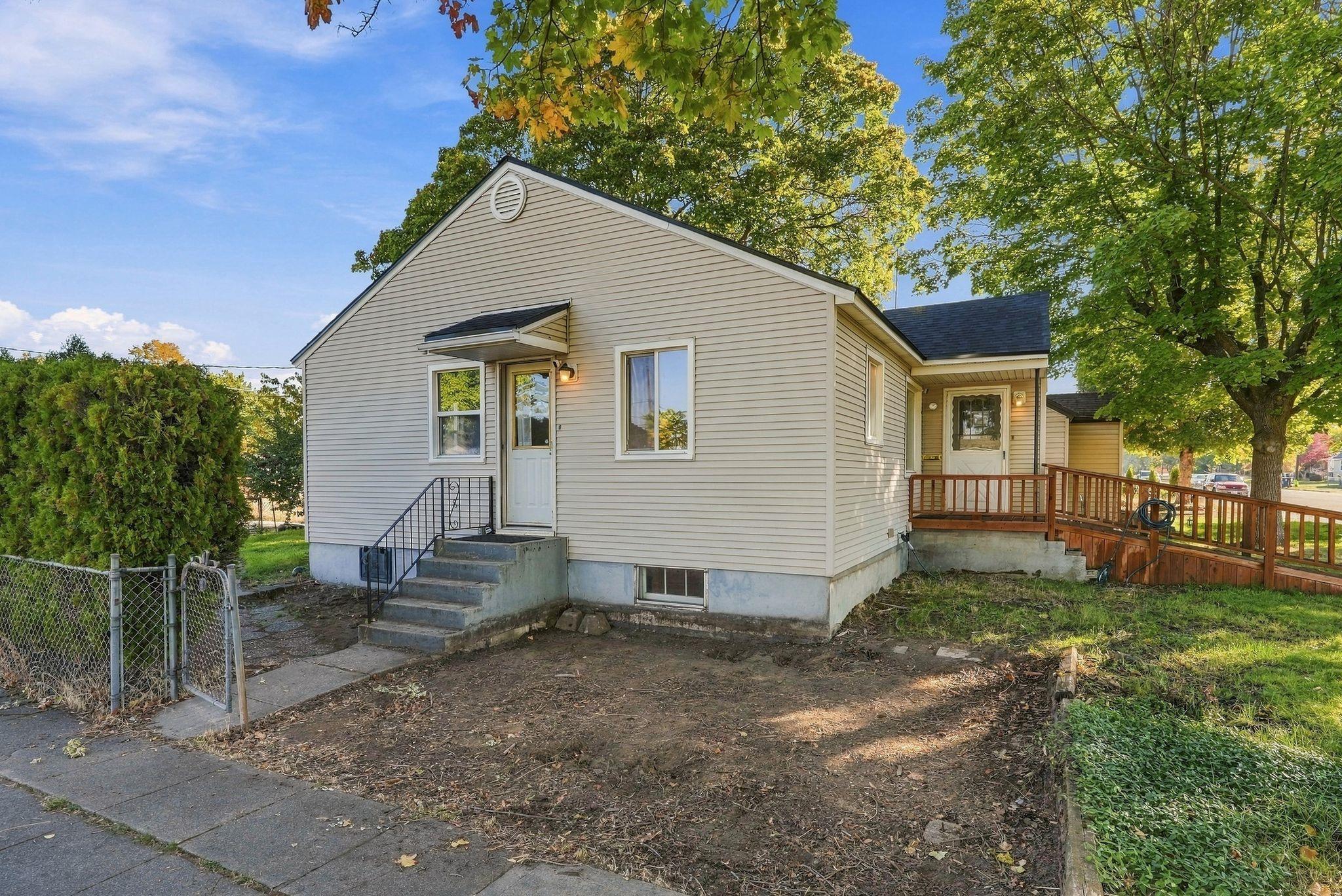 Light-sided single-story house with front steps and a wooden side ramp beneath mature trees.