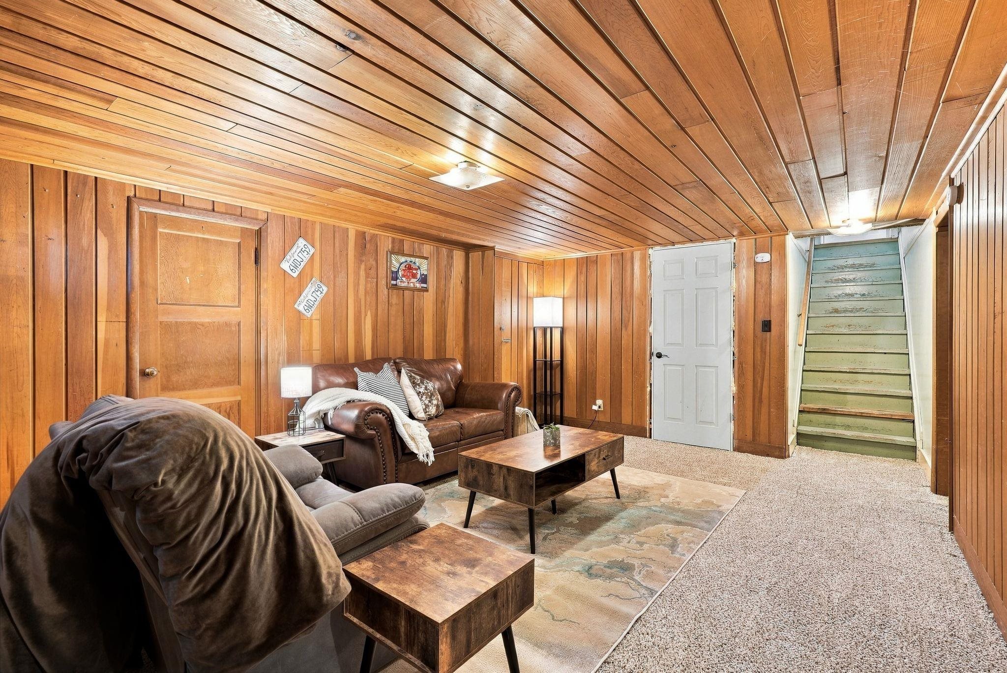 Furnished wood-paneled living room with brown sofas, a coffee table, and stairs.