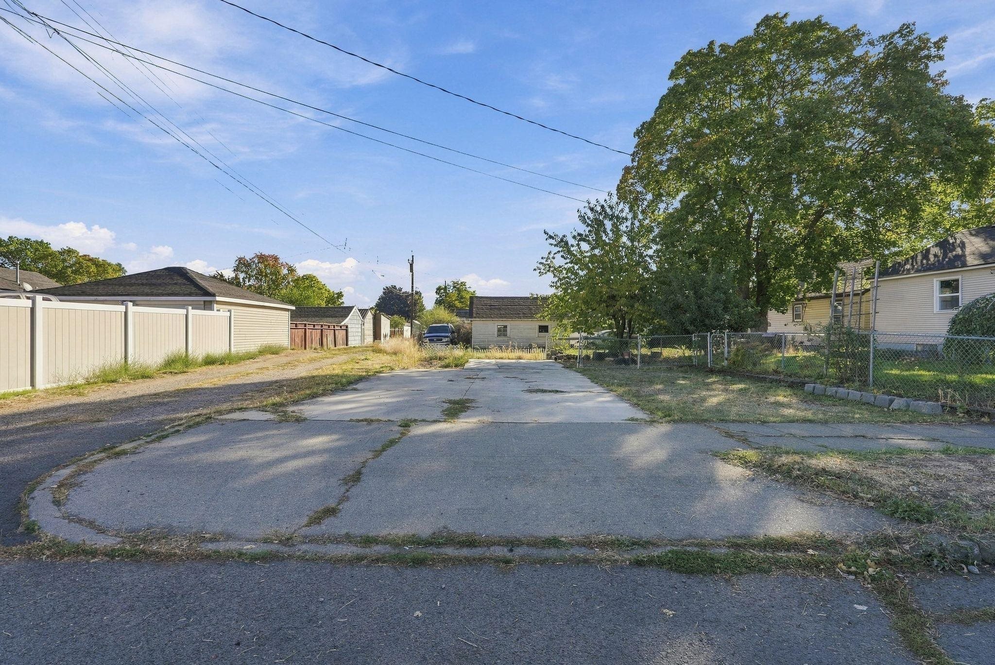 Paved driveway between neighboring garages, bordered by fences and a large shade tree.
