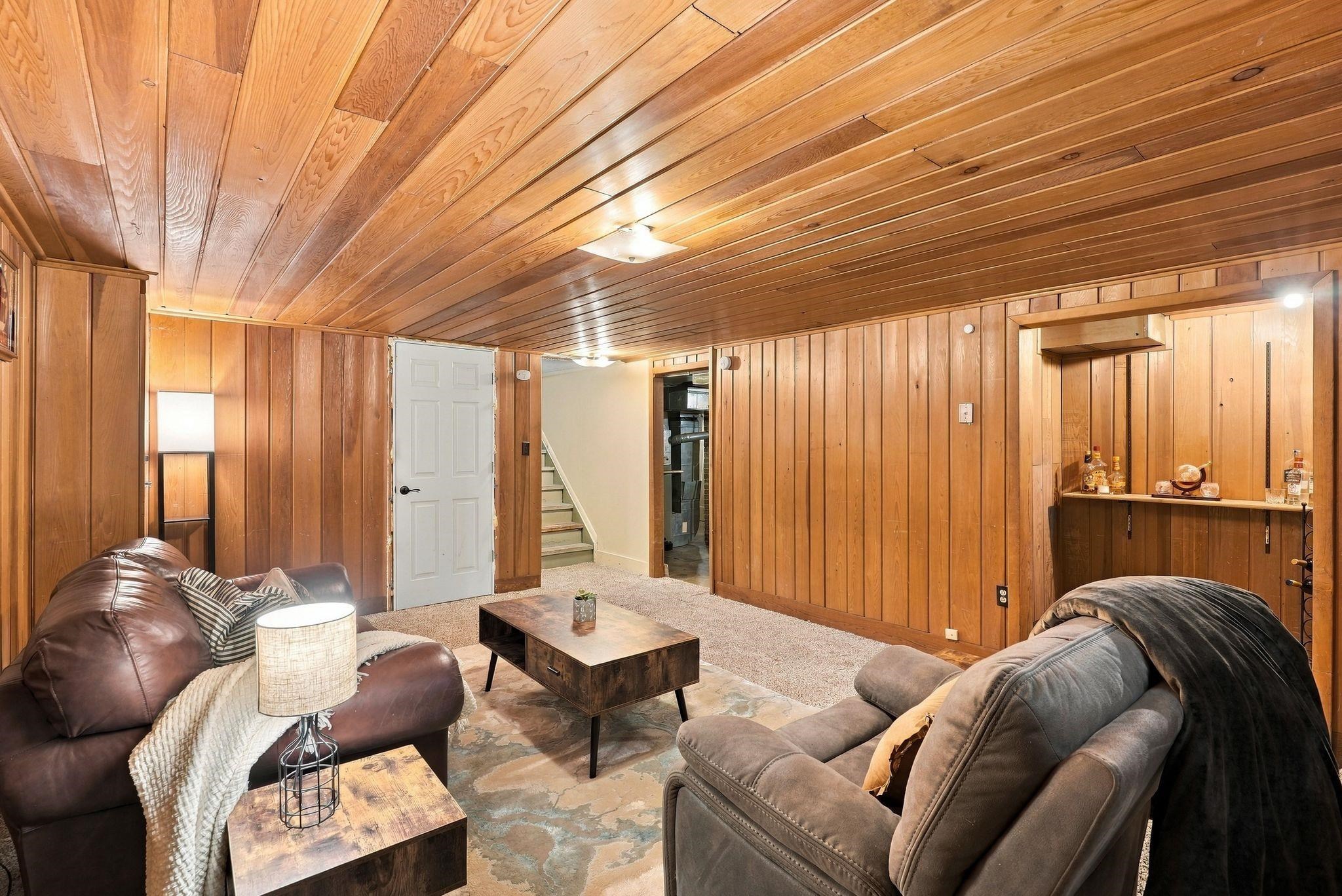 Furnished basement living room with wood paneling, leather sofas, and a small built-in bar.