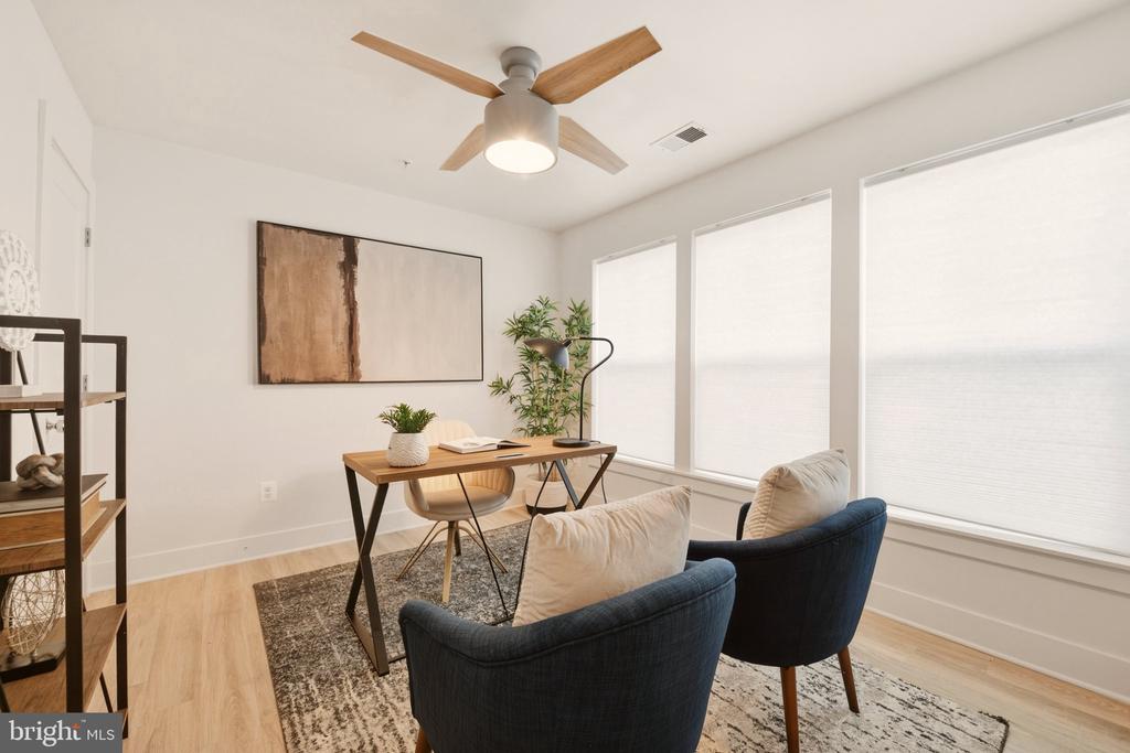 Staged home office with a wood desk, navy armchairs, and bright shaded windows.