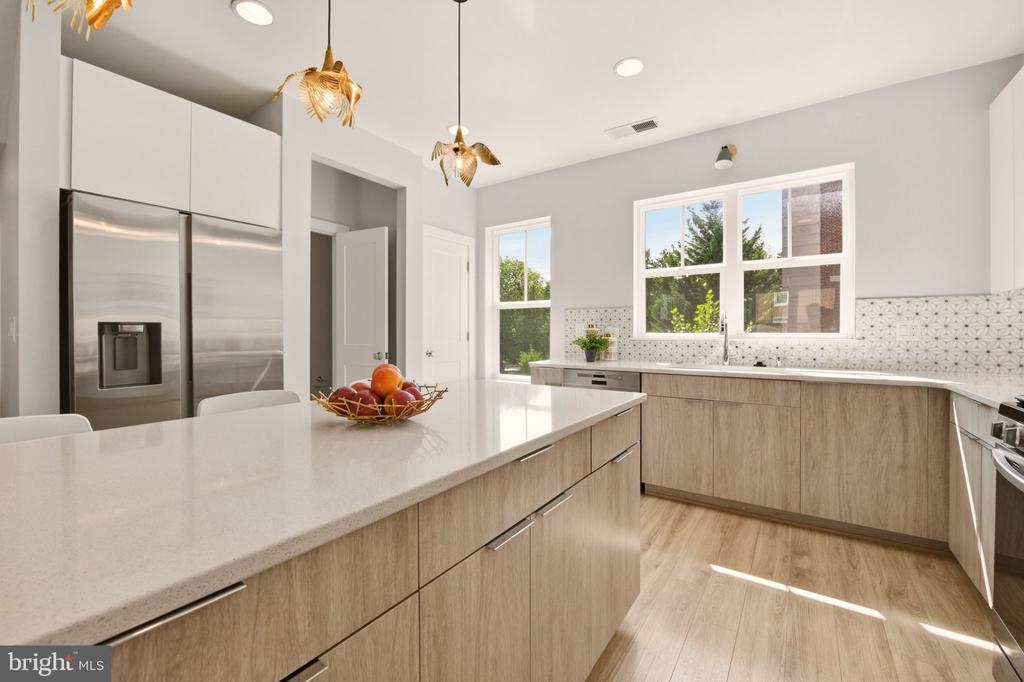 Renovated kitchen with a large white island, light wood cabinets, and stainless steel refrigerator.