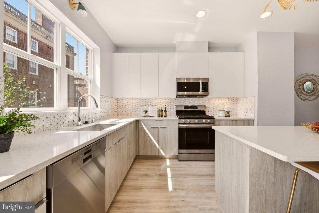 Kitchen with a large white island, stainless steel appliances, and tall sunlit windows.