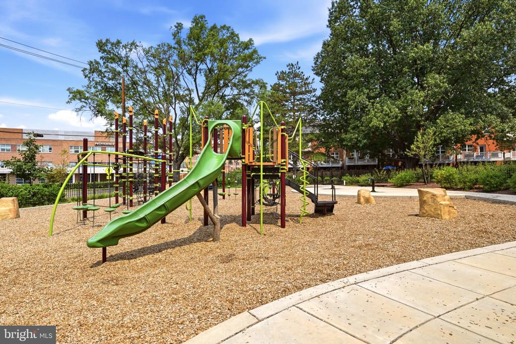 Neighborhood playground with a green slide and climbing structures beneath mature trees.