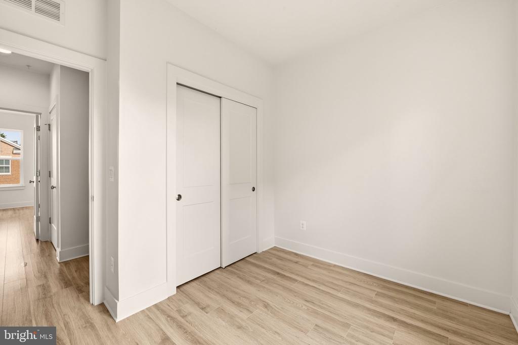 Empty room with light wood flooring and two white closet doors beside an open hallway.