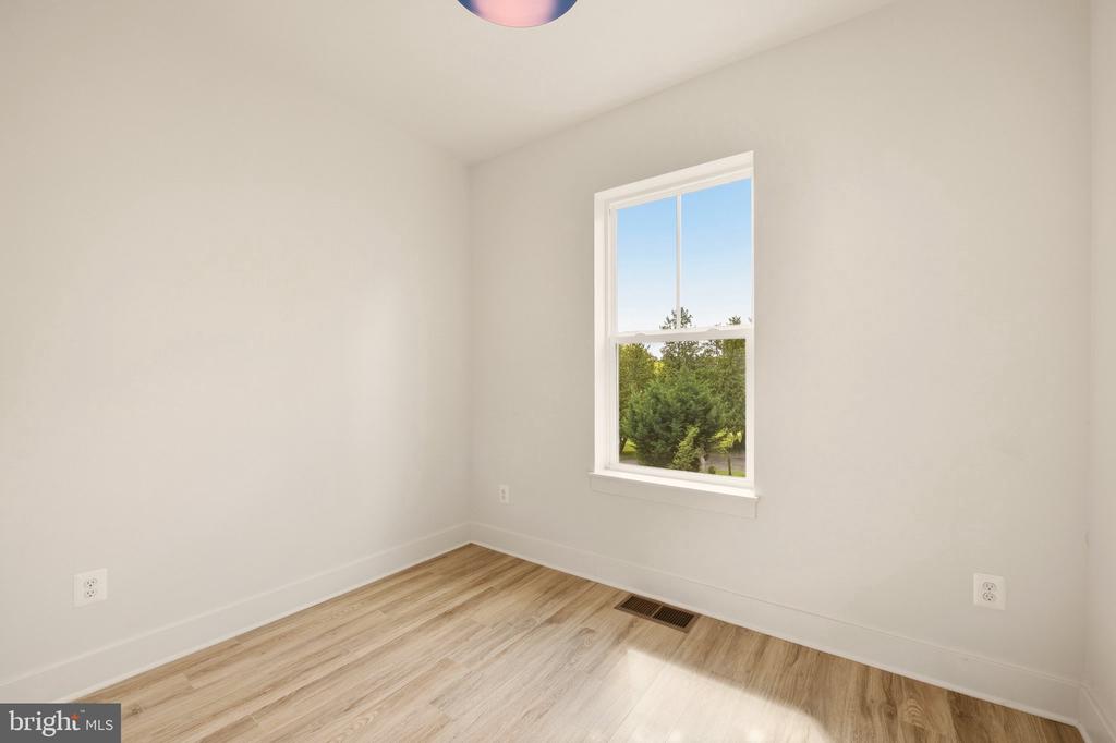 Empty room with light wood-look flooring and a window overlooking green trees.