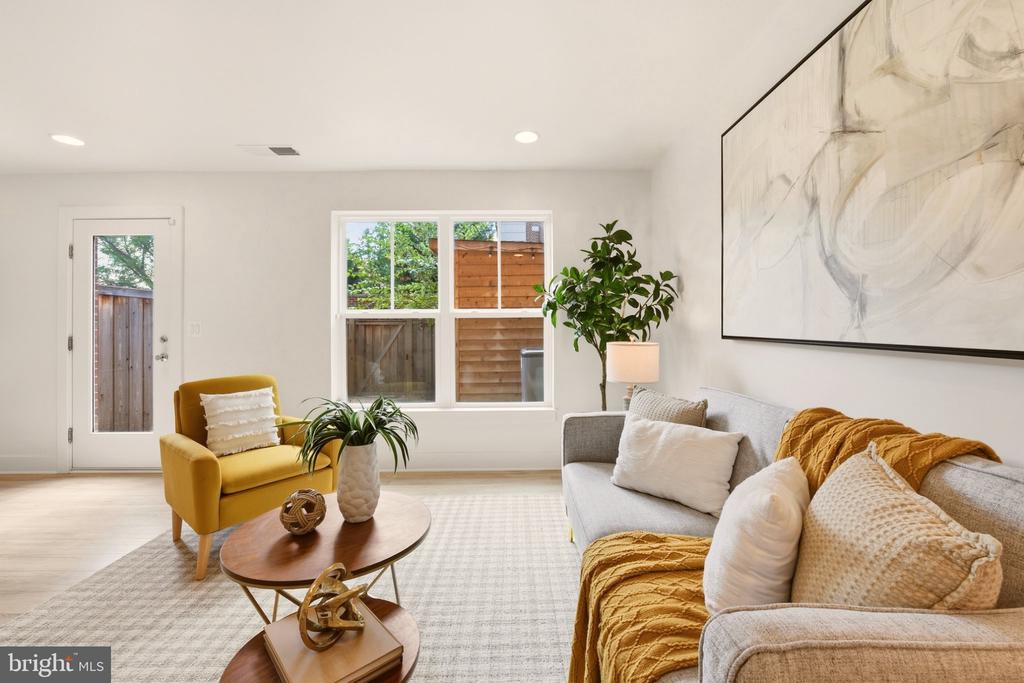 Staged living room with a gray sofa, mustard-yellow armchair, and windows facing a fenced yard.