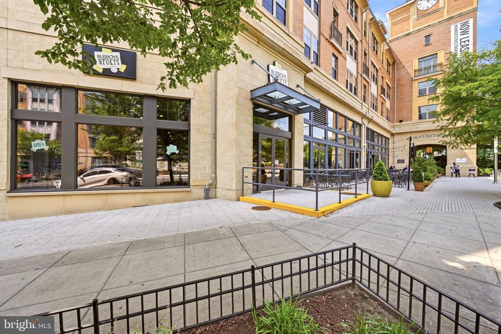 Multi-story brick building with storefront windows, a covered entrance, and a paved courtyard.