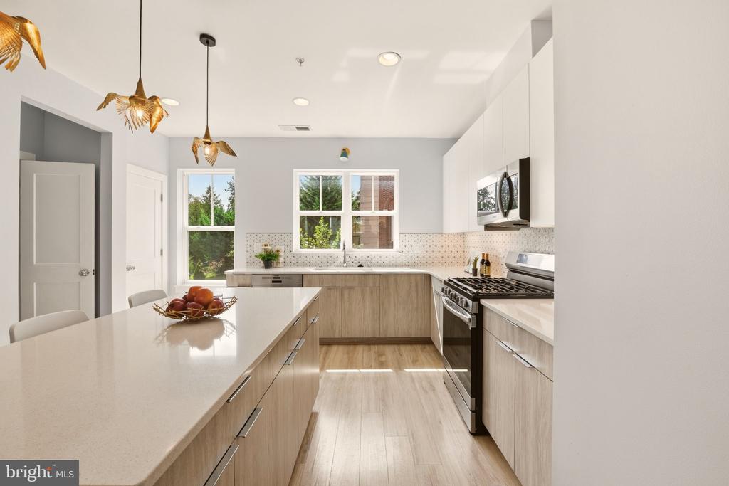Bright kitchen with a large island, light wood cabinets, stainless appliances, and gold pendant lights.