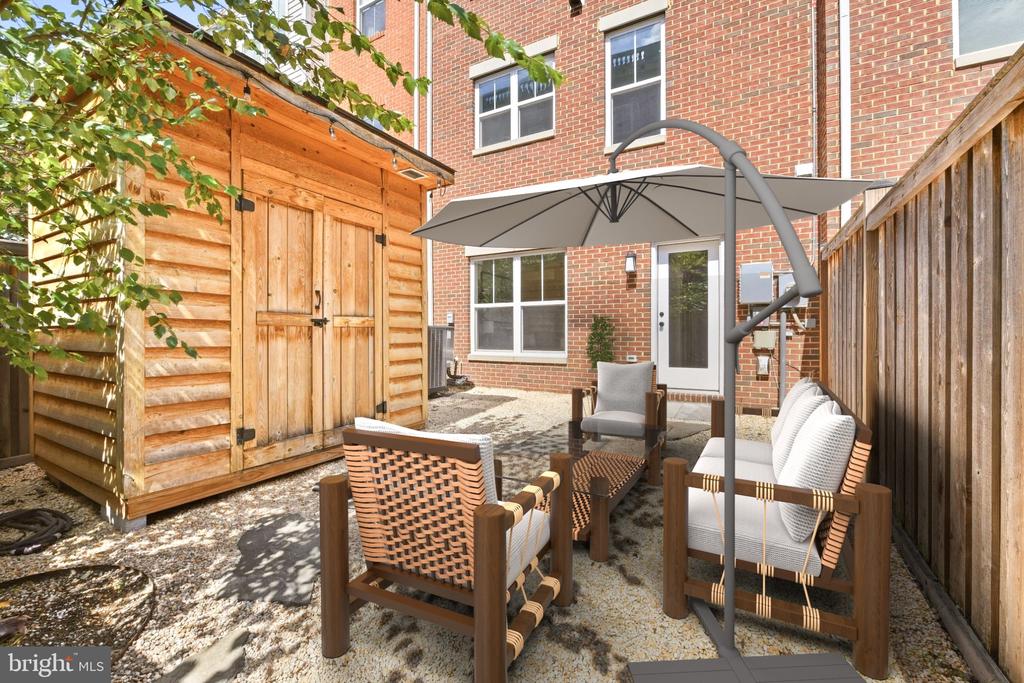 Fenced patio with a wooden shed and outdoor seating beneath a large umbrella.