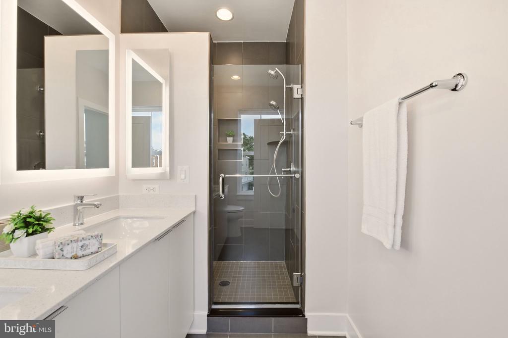Modern bathroom with a white vanity, large mirrors, and a glass-enclosed dark-tile shower.