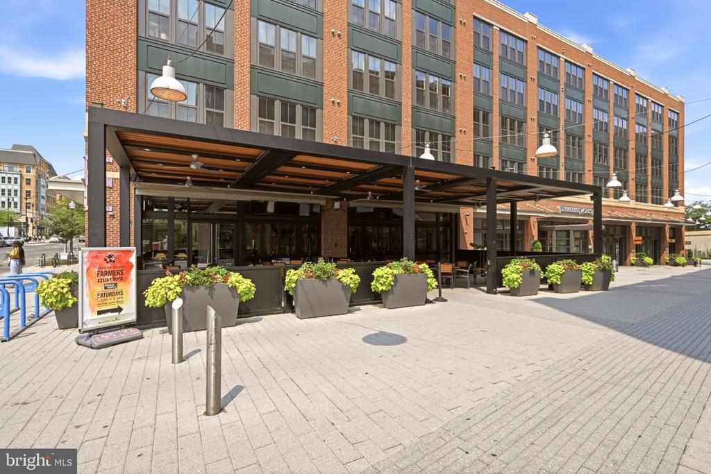 Brick building with a covered sidewalk dining area and rows of planters.