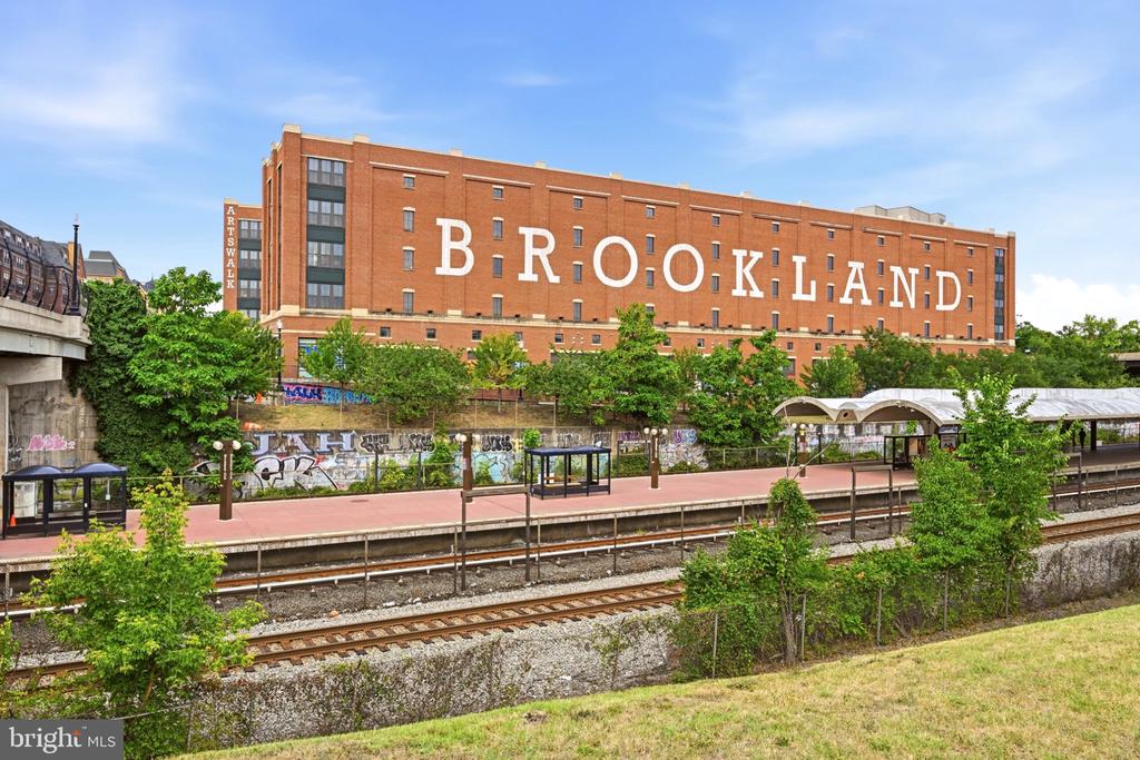 Brookland building behind a rail station platform, tracks, and trees.