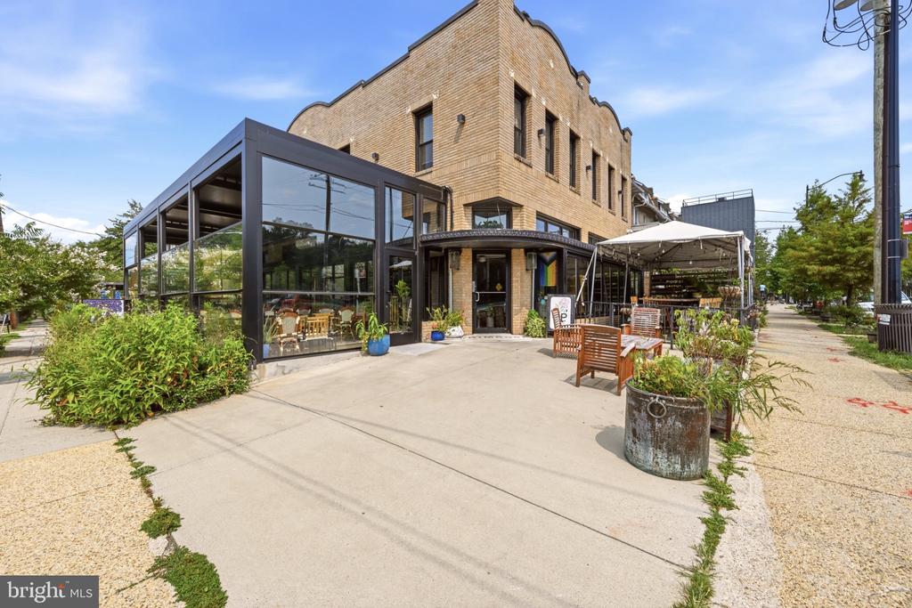 Tan brick commercial building with a glass-enclosed patio and outdoor seating.