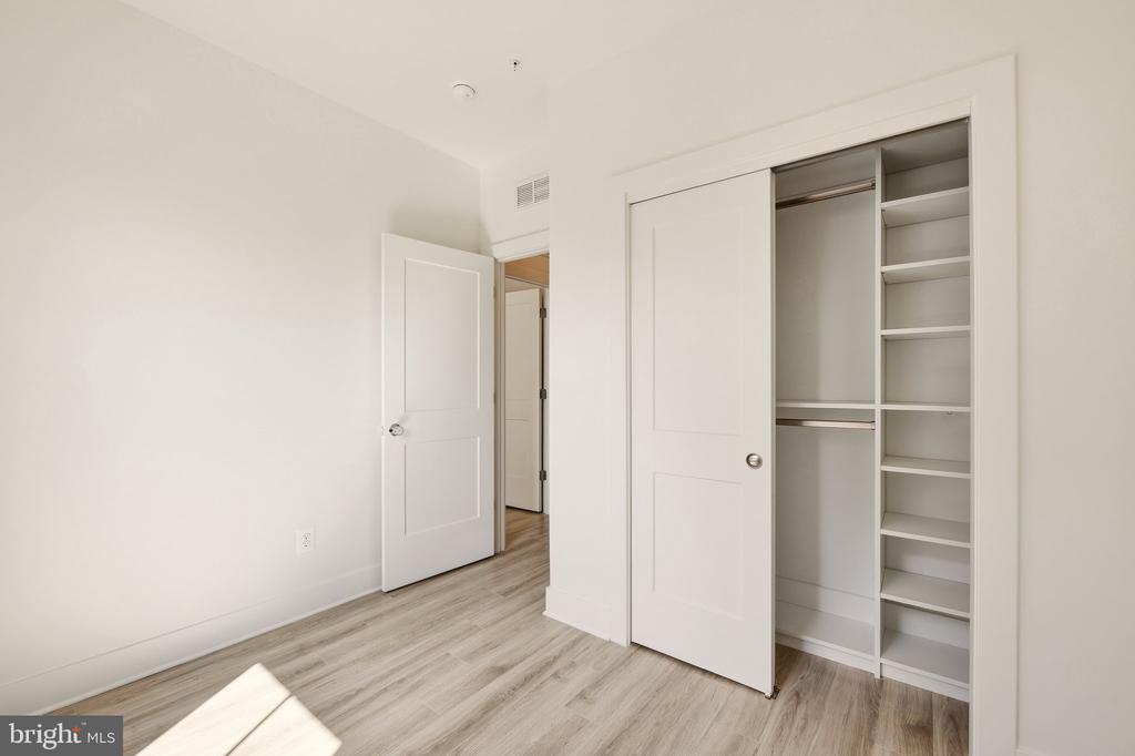 Empty bedroom with light wood-look flooring and an open built-in closet with shelves and hanging space.