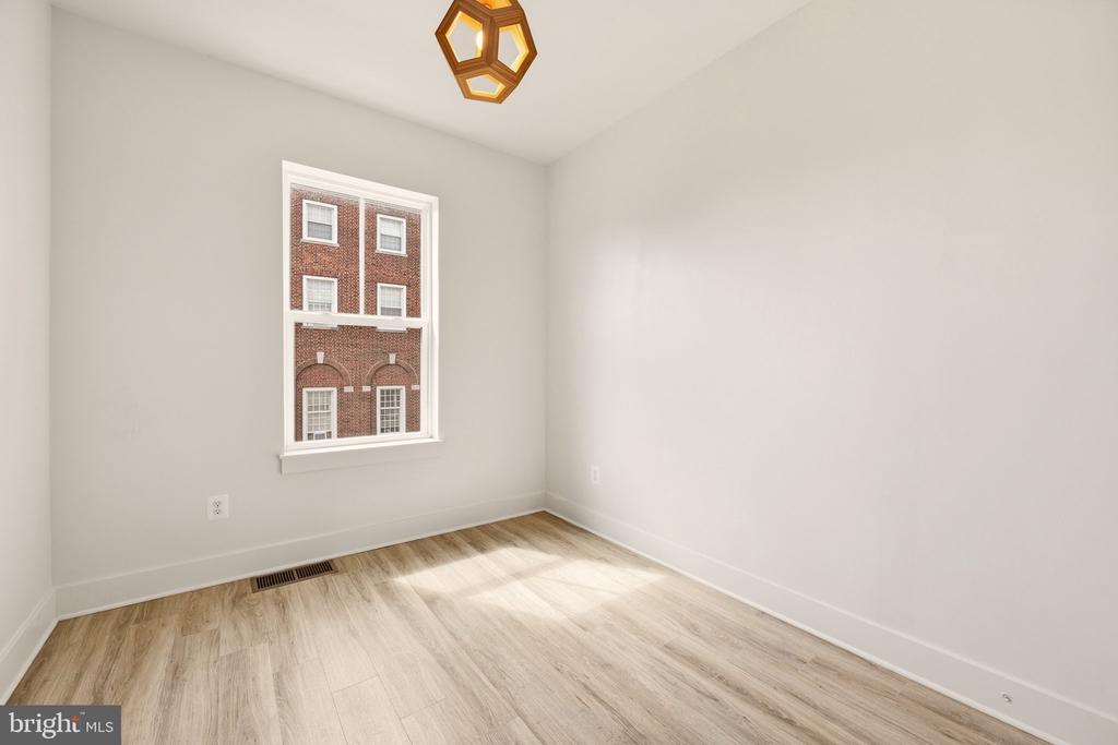 Empty room with pale wood-look flooring, a tall window, and a geometric pendant light.