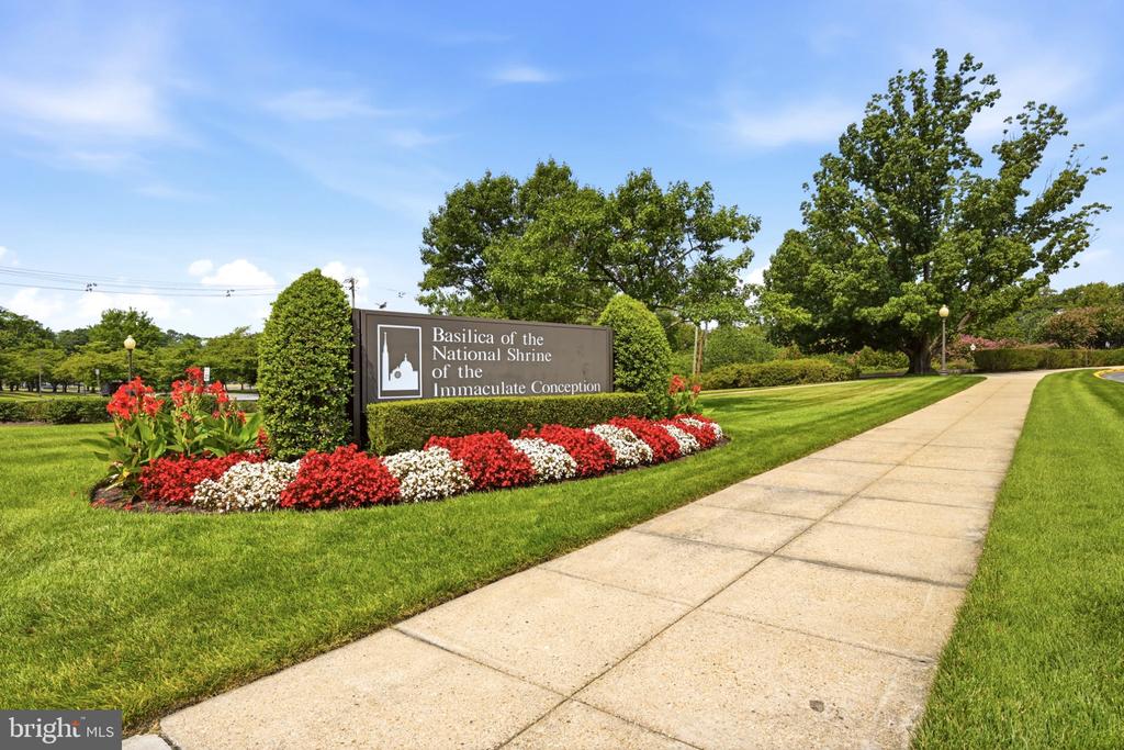 Sign for the Basilica of the National Shrine of the Immaculate Conception beside flower beds and a paved walkway.