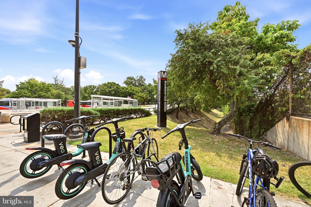 Brookland-CUA Metro station sign beside bike-share bicycles and a tree-lined path.