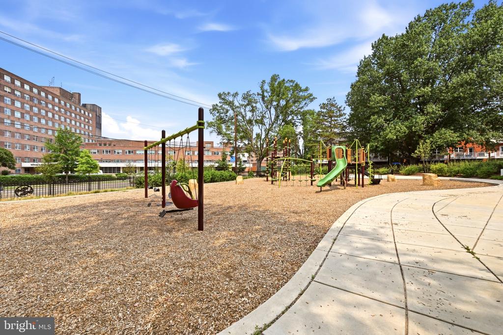Playground with swings and green slides beside a curved concrete walkway.