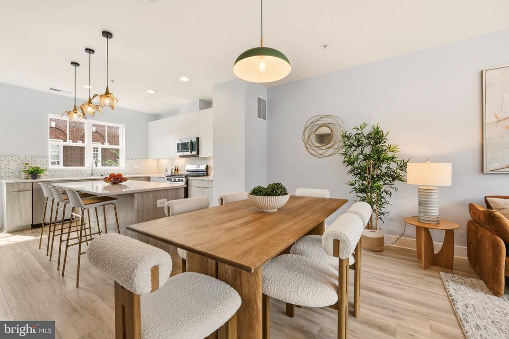Open-plan dining room and kitchen with a long wooden table, upholstered chairs, and pendant lights.