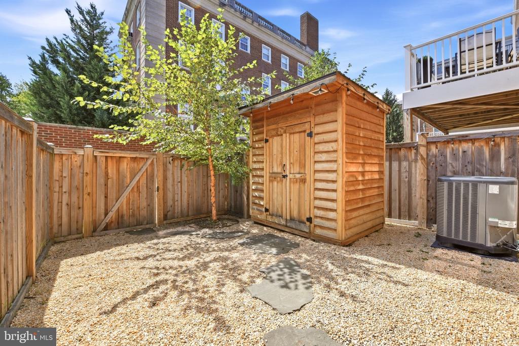 Fenced gravel backyard with a wooden storage shed and raised deck.