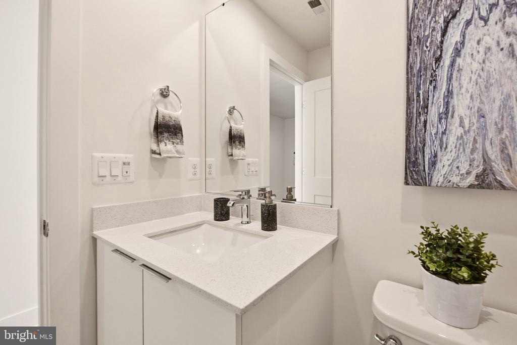 Bathroom vanity with a speckled white countertop, large mirror, and potted plant on the toilet.