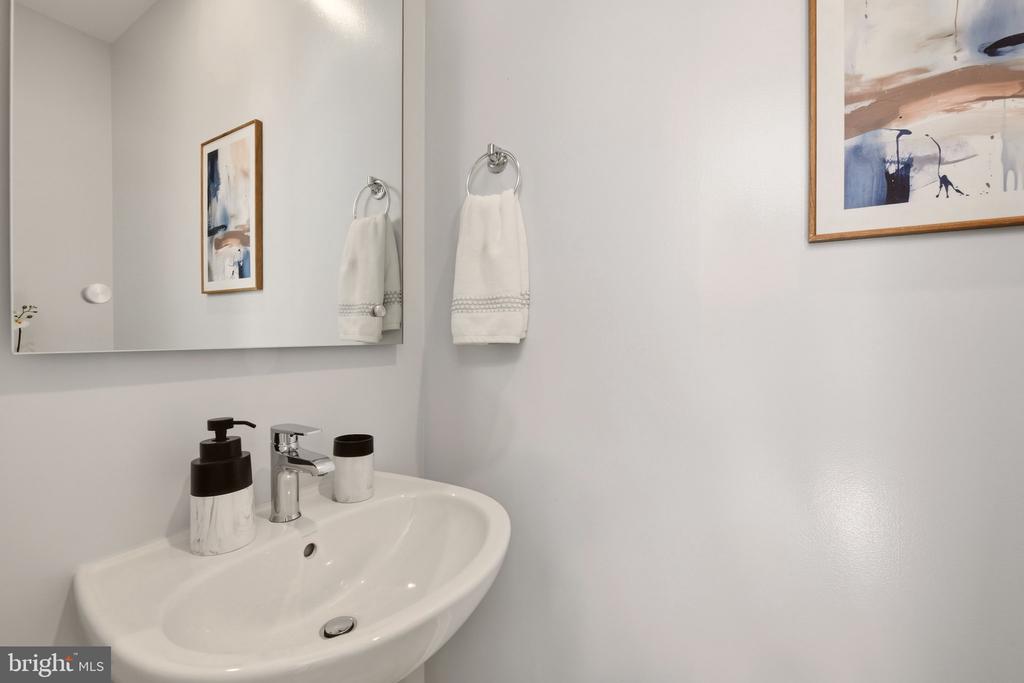 Bathroom sink with chrome faucet, countertop accessories, and white towels beside a large mirror.