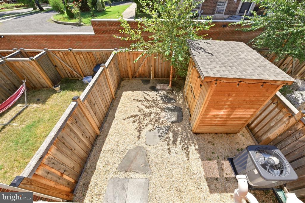Fenced backyard with a gravel patio, wooden shed, stepping stones, and a hammock.
