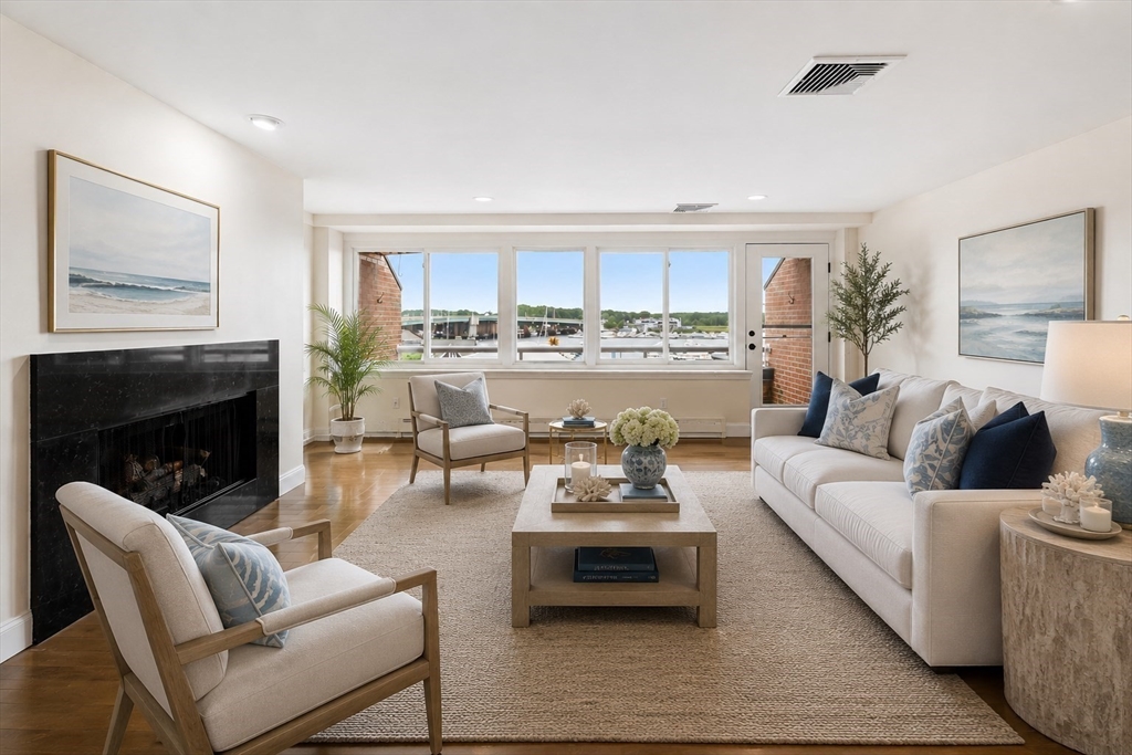 Staged living room with a black fireplace and wide windows overlooking boats and water.