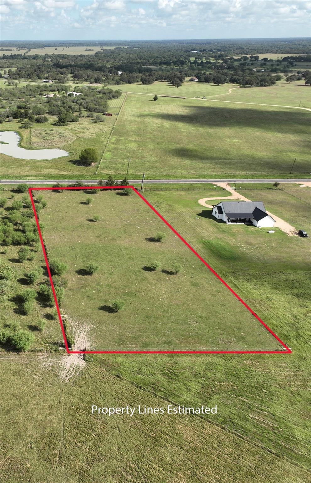 Aerial view of grassy parcel outlined in red beside a road, with a nearby pond.