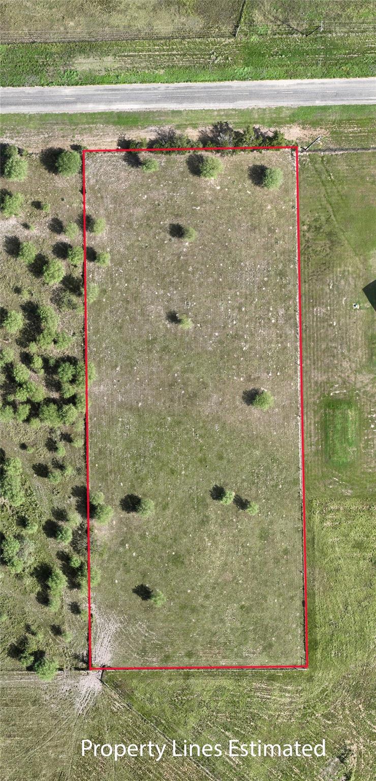Aerial view of a grassy vacant lot outlined in red beside a road.