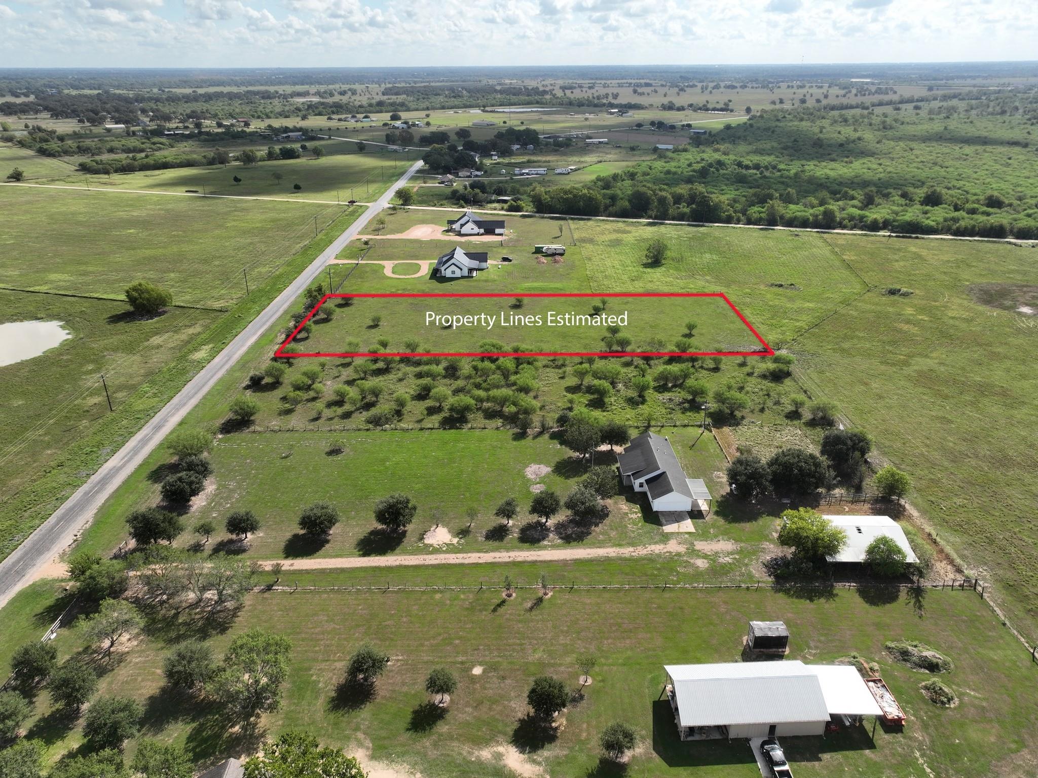 Aerial view of a grassy rural lot outlined in red beside a paved road.