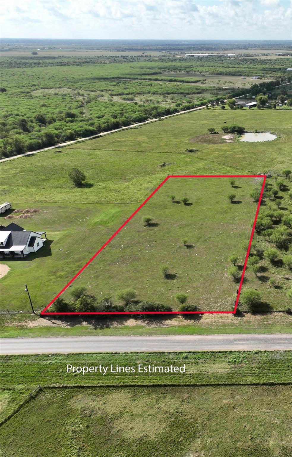 Aerial view of a vacant pasture parcel outlined in red beside a road.