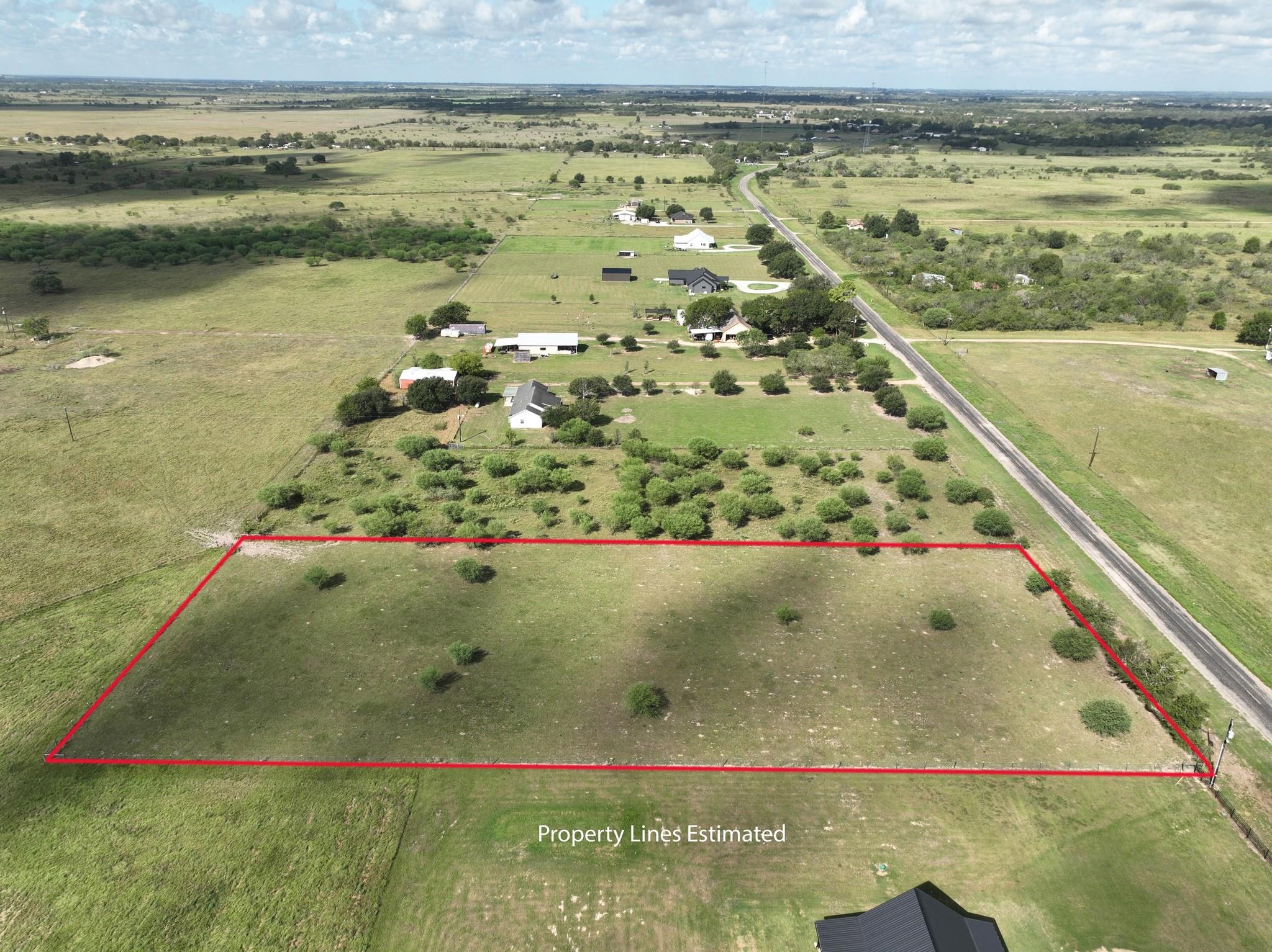 Aerial view of a grassy rural parcel outlined in red beside a paved road.