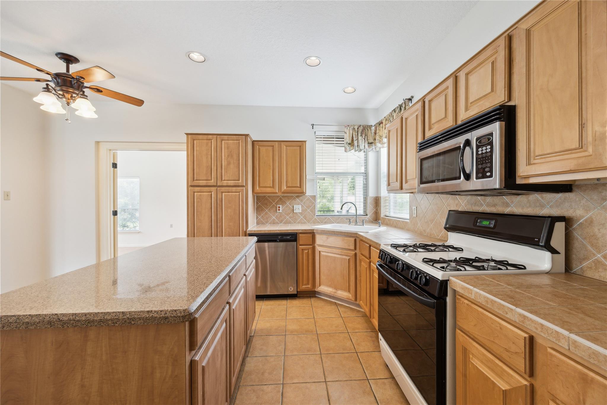 Kitchen with a granite-topped island, honey-colored cabinets, and a gas range beneath a microwave.