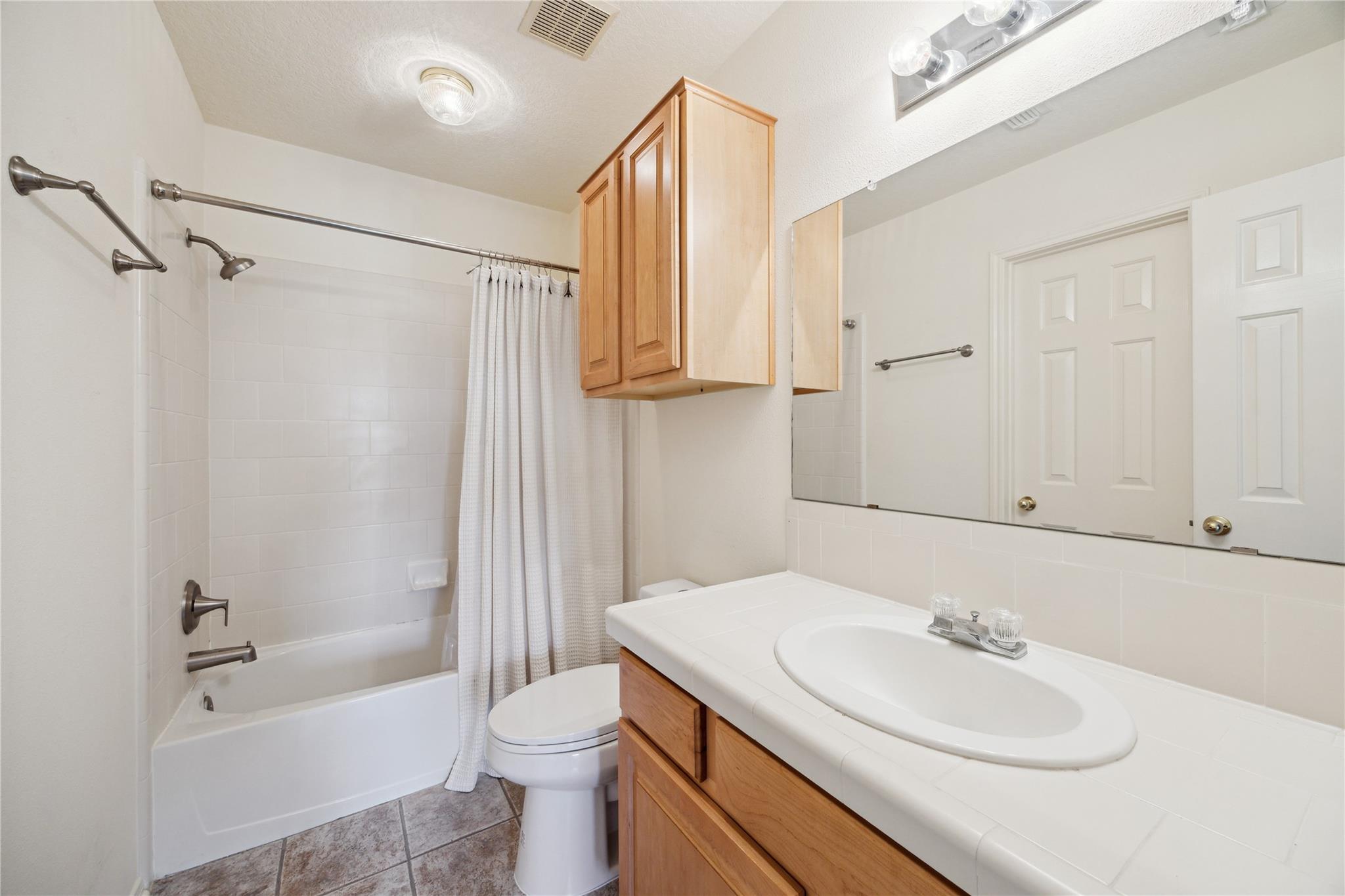 Bathroom with a curtained bathtub, toilet, and wood vanity with a large mirror.