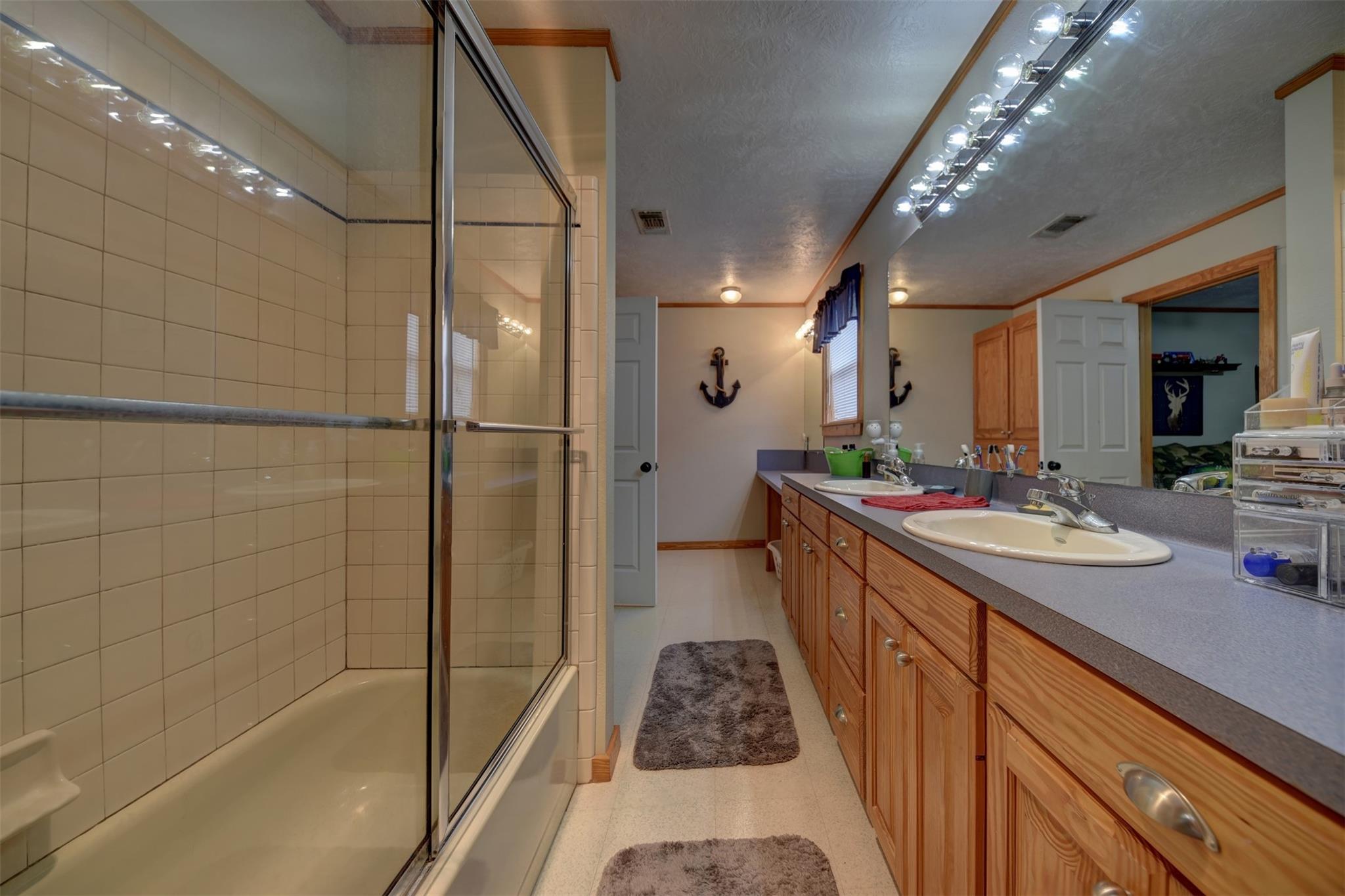 Bathroom with a glass-enclosed tiled shower and long double-sink vanity.