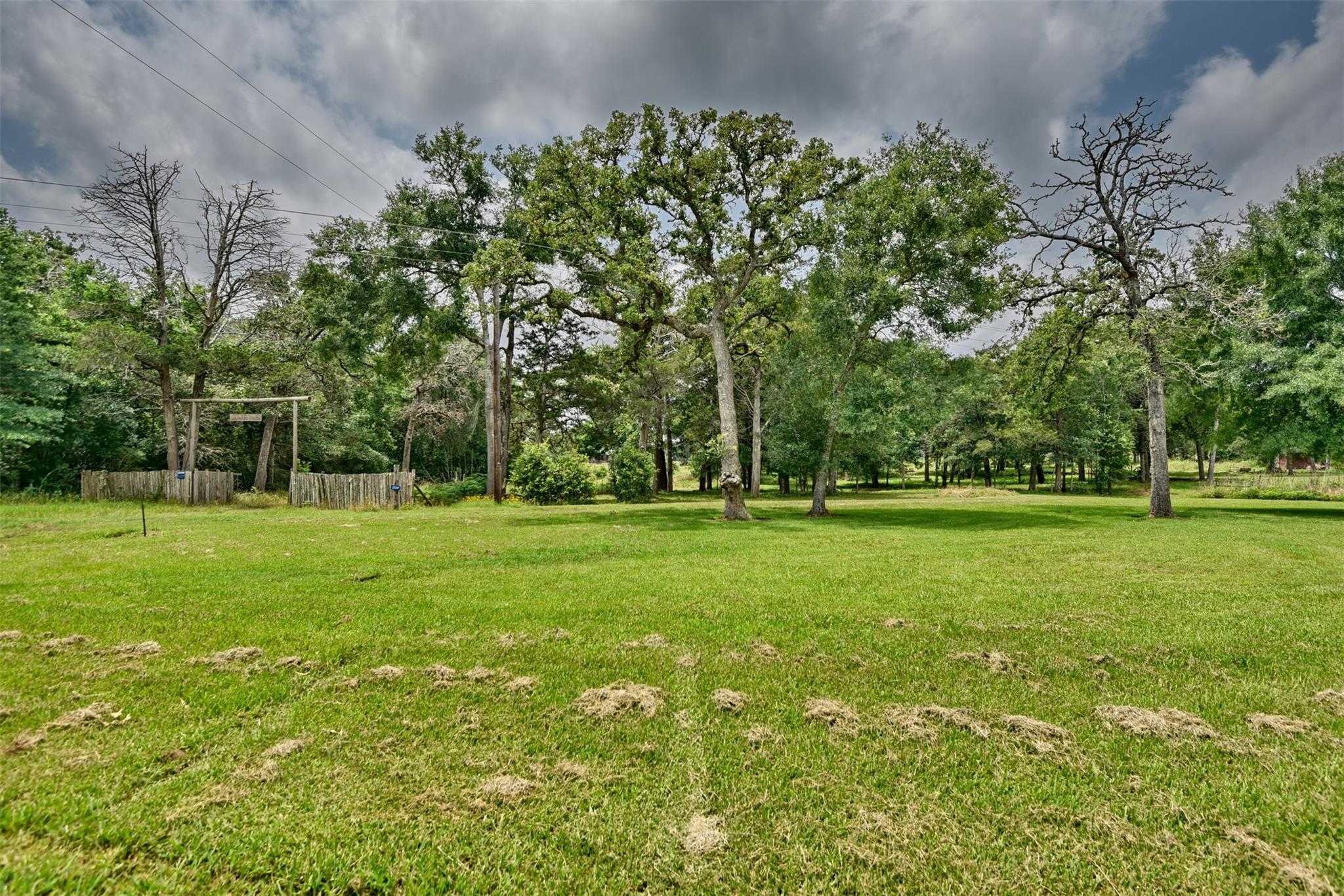 Grassy property with mature trees and a rustic wooden entrance fence.