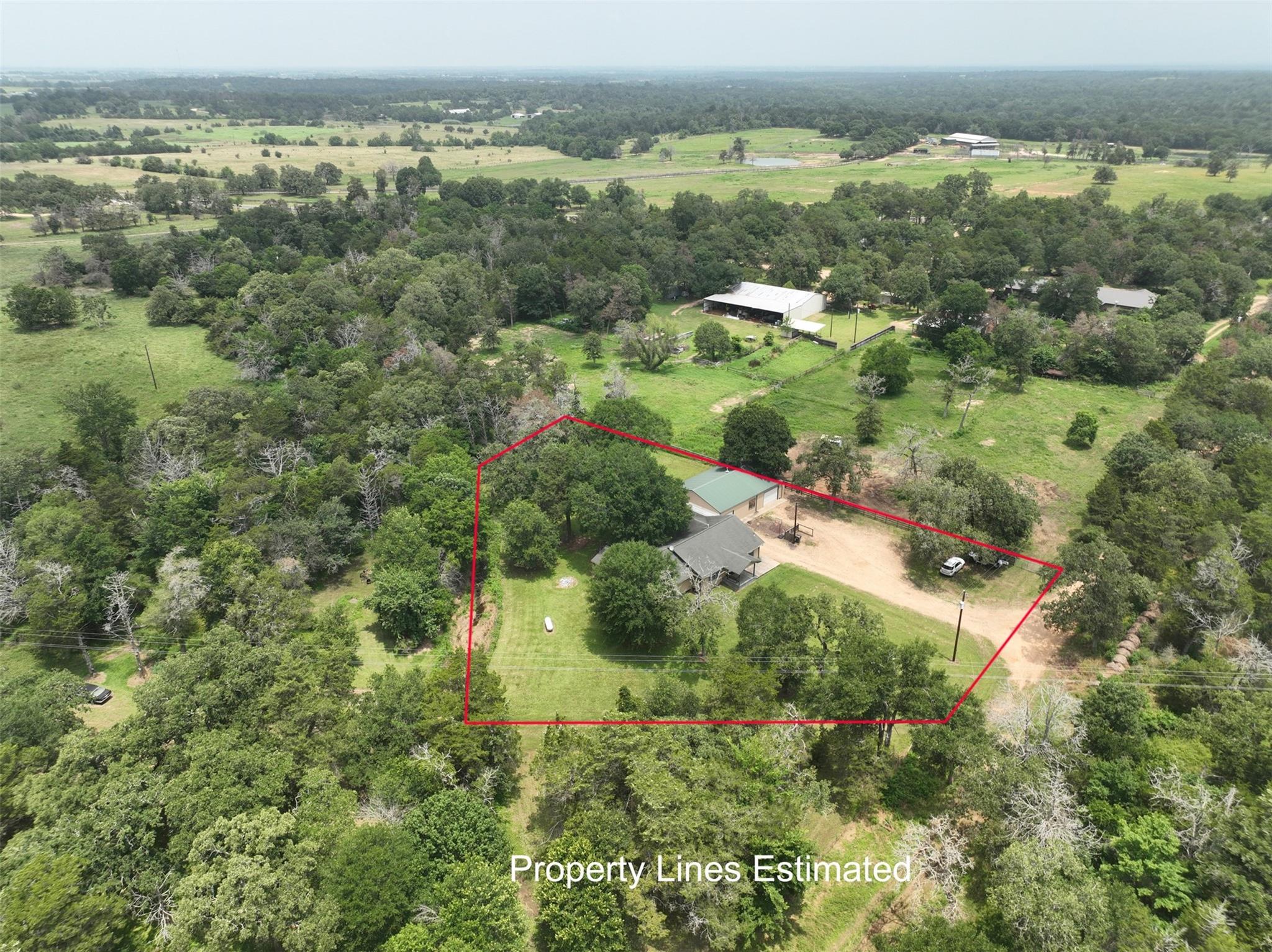 Aerial view of a wooded rural property outlined in red, with a house, outbuilding, and gravel drive.