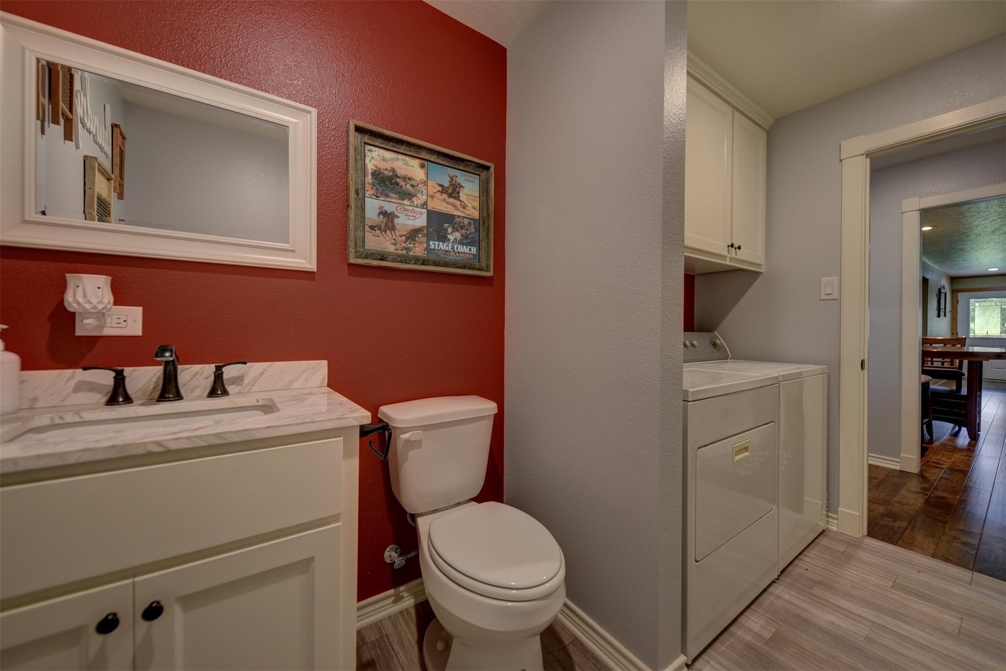 Bathroom with red accent wall, white vanity, toilet, and adjoining laundry area.
