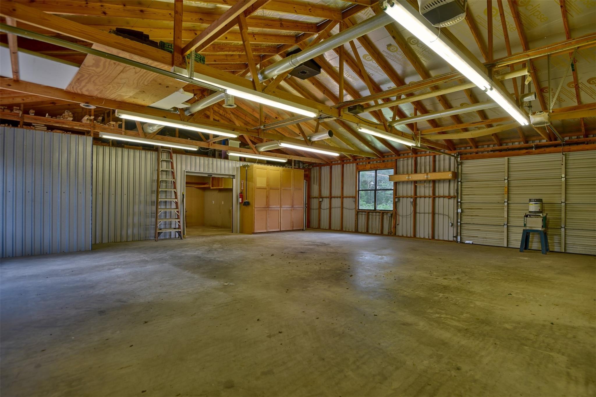 Spacious metal garage with exposed wooden trusses, concrete floor, and overhead doors.