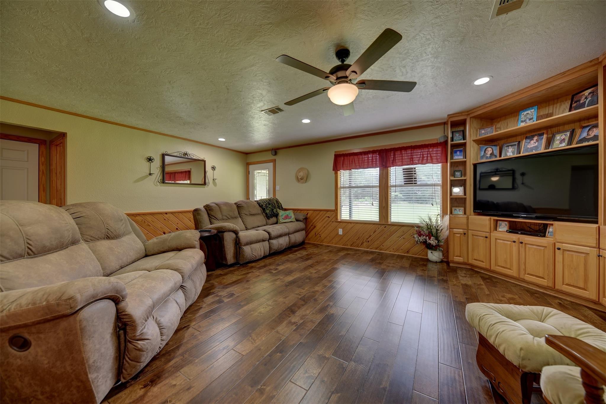 Living room with recliner sofas, wood-look flooring, and a built-in entertainment center.