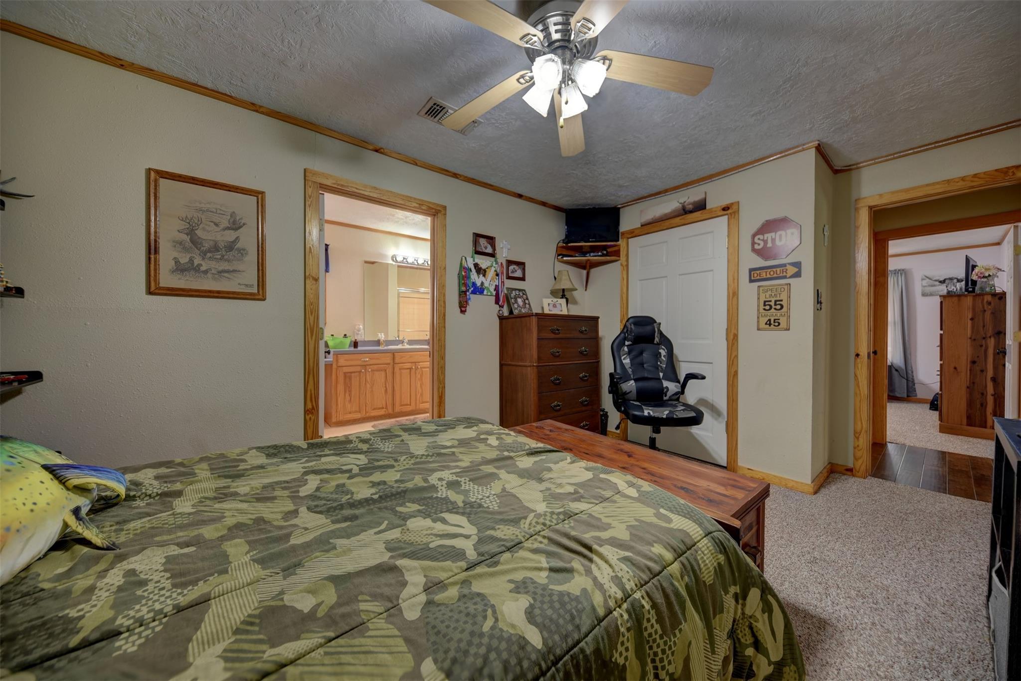 Bedroom with camouflage bedding, wood trim, and open doorways to a bathroom and another room.