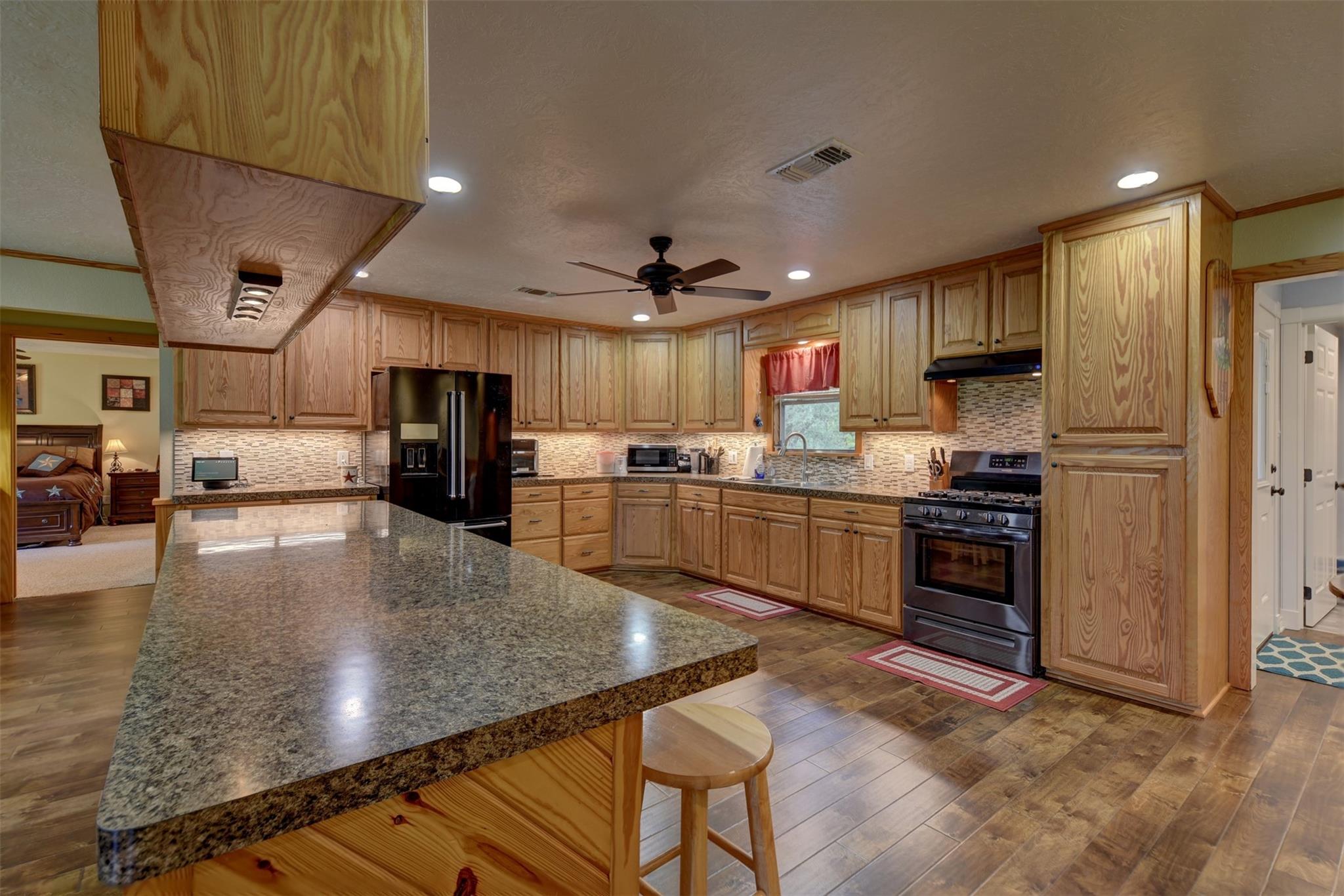 Kitchen with natural wood cabinets, granite island, black appliances, and a bedroom visible through the doorway.