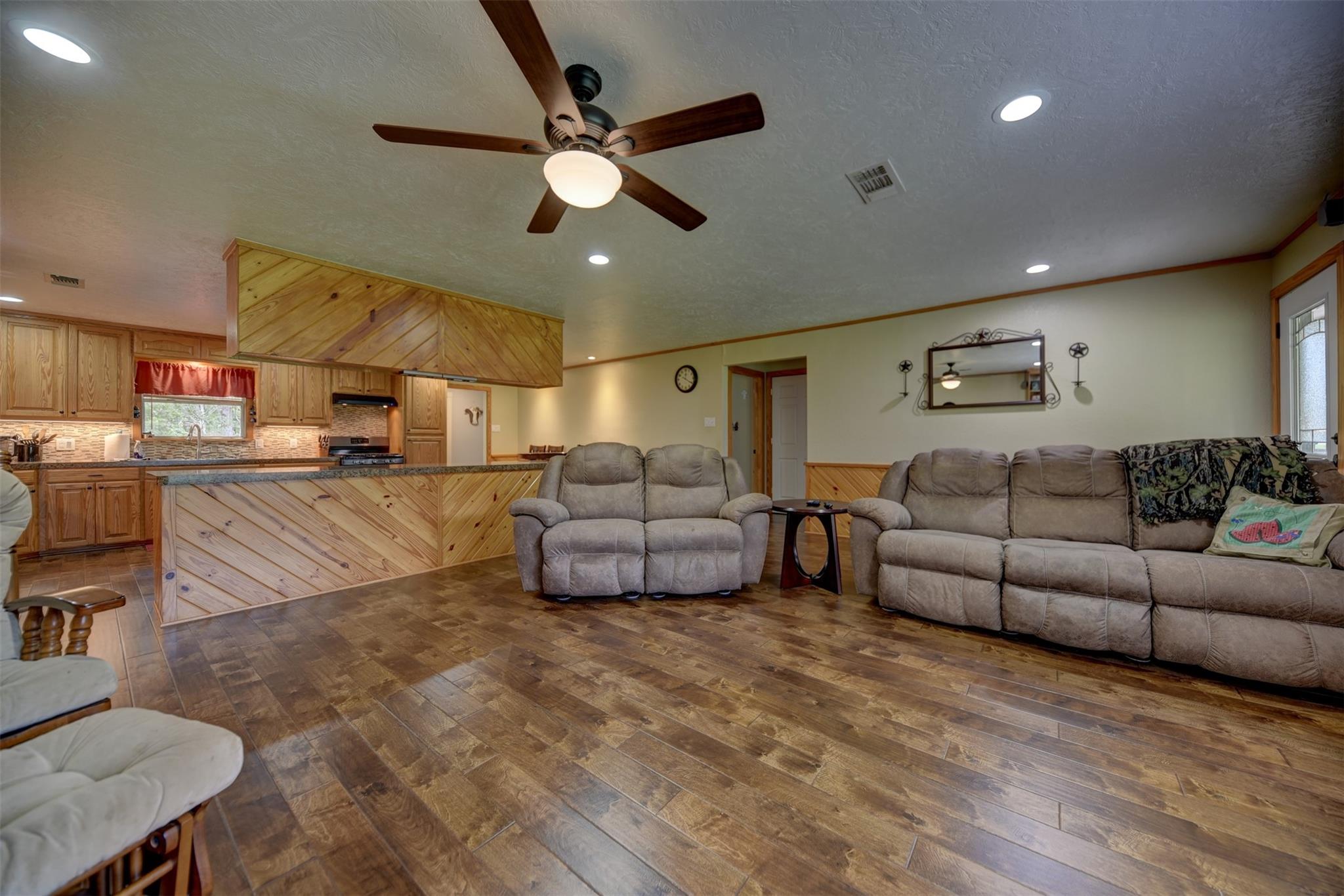 Open living room and kitchen with wood cabinetry, a paneled breakfast bar, and reclining sofas.