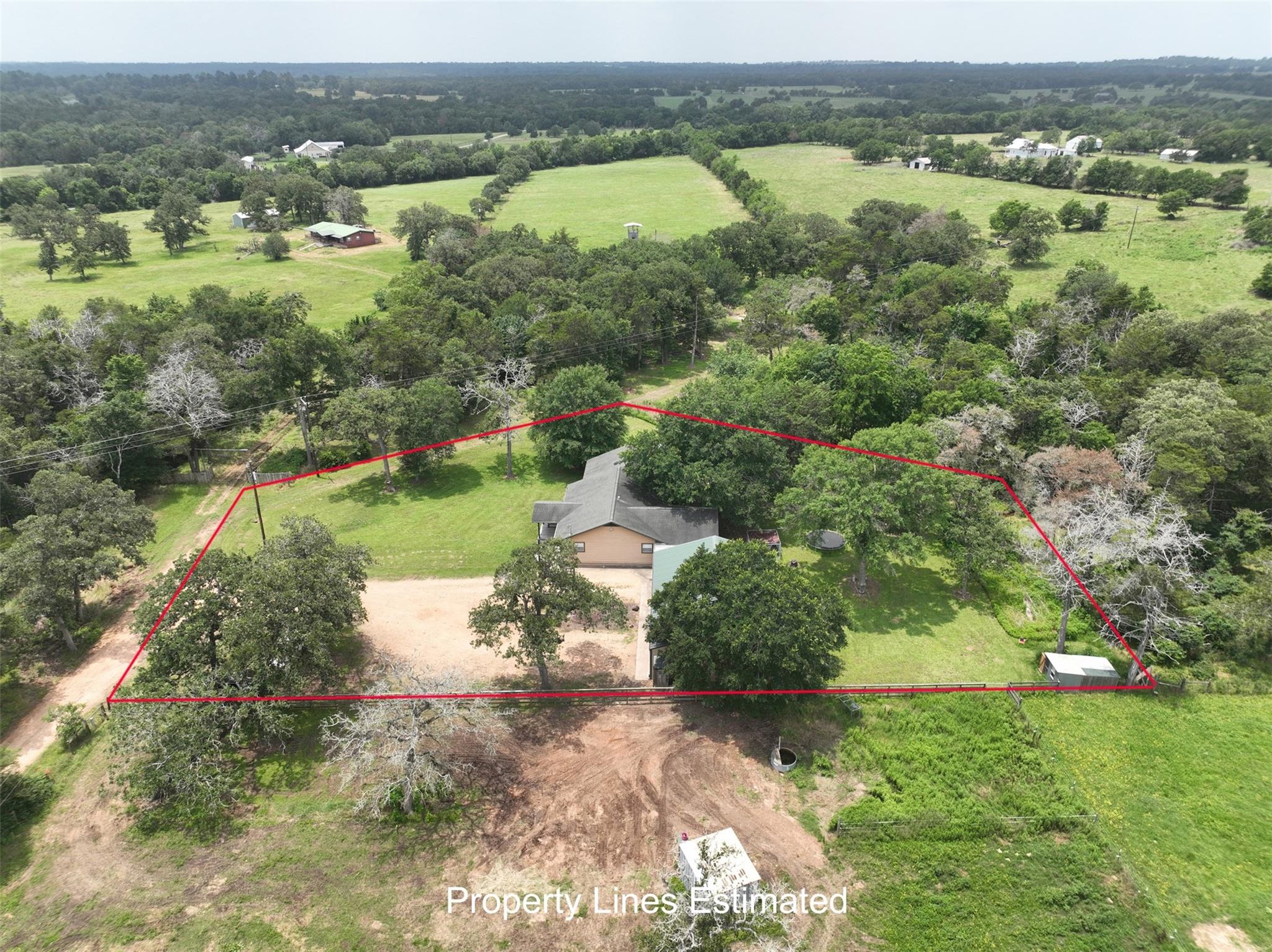 Aerial view of a tree-shaded rural home and lot outlined in red.